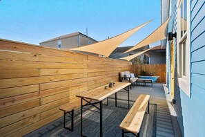 Eine Holzterrasse mit Bänken und einem Tisch, ein Schwimmbecken und ein blaues Gebäude im Hintergrund.