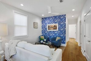 Una sala de estar moderna con un sofá blanco, un sillón azul, una mesa de centro y un ventilador de techo.