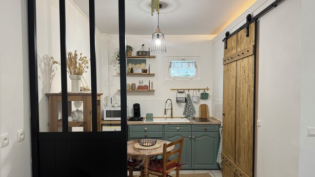 A kitchen with a dining area, a wooden cabinet, a sliding barn door, and a hanging light fixture. - Studio Normand (Dives-sur-Mer)