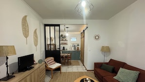 A living room with a TV, sofa, and coffee table. There is a kitchen in the background with a dining area. - Studio Normand (Dives-sur-Mer)