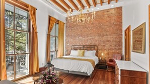 Un dormitorio con una cama grande, suelo de madera, pared de ladrillo y un candelabro.