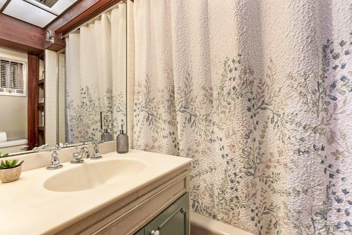 Casa de banho com lavatório, espelho e cortina de chuveiro estampada com flores.