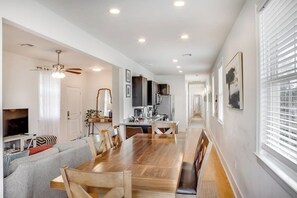 A modern kitchen with a central island, a dining area with a wooden table and chairs, and a living room with a sofa and television. - NOLA Sanctuary Summar (New Orleans)