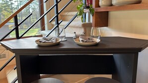 Une table à manger, dressée avec des assiettes, des couverts et des verres, est placée près d’un escalier, offrant une vue sur les arbres.