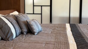 Un lit bien fait, avec une couvre-lit à motifs et des oreillers, une tête de lit en bois et un motif géométrique sur le mur en arrière-plan.