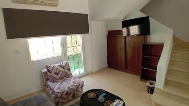 Una sala de estar con un sofá, una mesita, una escalera y un televisor montado en la pared.