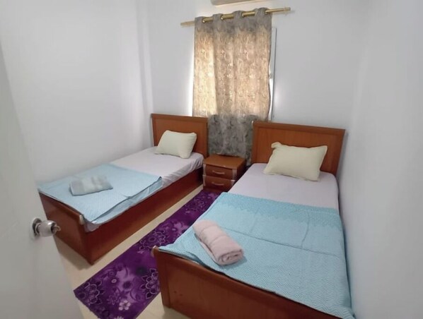 A small, clean room with two single beds, a wooden nightstand, and a purple floral runner.