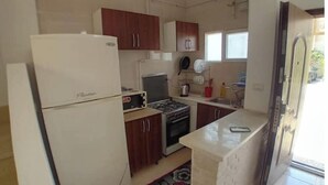 Cocina compacta con refrigerador, estufa, microondas y gabinetes de madera.