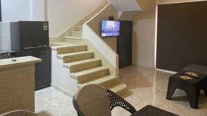 Una sala de estar moderna con una escalera, un televisor de pantalla plana montado en la pared, una mesita y una silla.