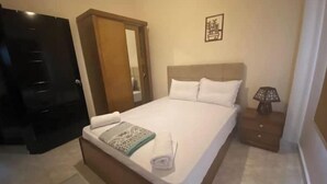Habitación de hotel con cama, mesita de noche, lámpara, puerta y un cuadro en la pared.