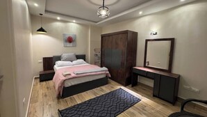 A bedroom with a bed, bedside tables, a wardrobe, a desk, a chair, a mirror, and a patterned rug. - 903 . Spacious 3BR Apt., 2 Baths, Gated Community (Al Sheikh Zayed)