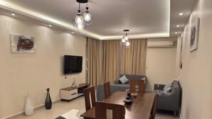 A modern living room with a dining table, sofa, and TV. - 903 . Spacious 3BR Apt., 2 Baths, Gated Community (Al Sheikh Zayed)