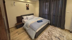 A bedroom with a bed, a headboard, a wall-mounted artwork, a ceiling light, and a window with curtains. - 803 . Spacious 3BR Apt., 2 Baths, Gated Community (Al Sheikh Zayed)