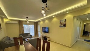 A modern living room with a dining table, sofa, and TV. - 803 . Spacious 3BR Apt., 2 Baths, Gated Community (Al Sheikh Zayed)
