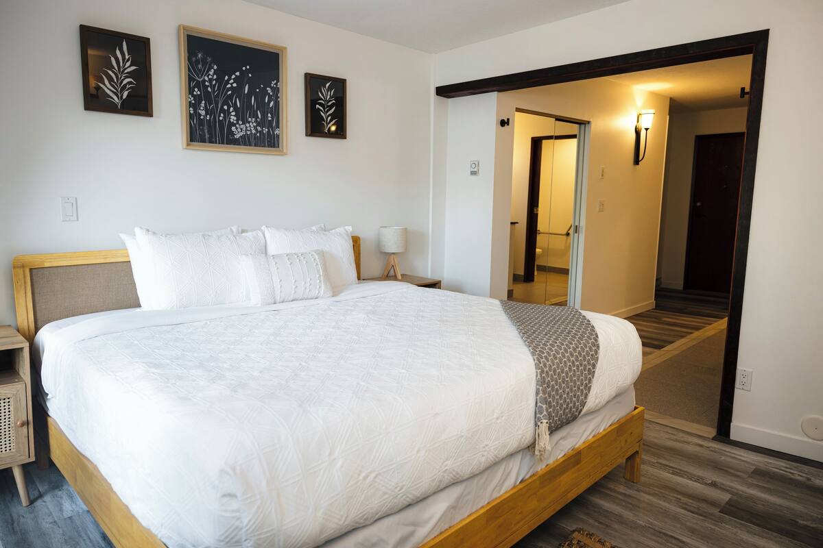 A neatly made bed with a wooden headboard, a bedside table with a lamp, and a wall-mounted picture frame.