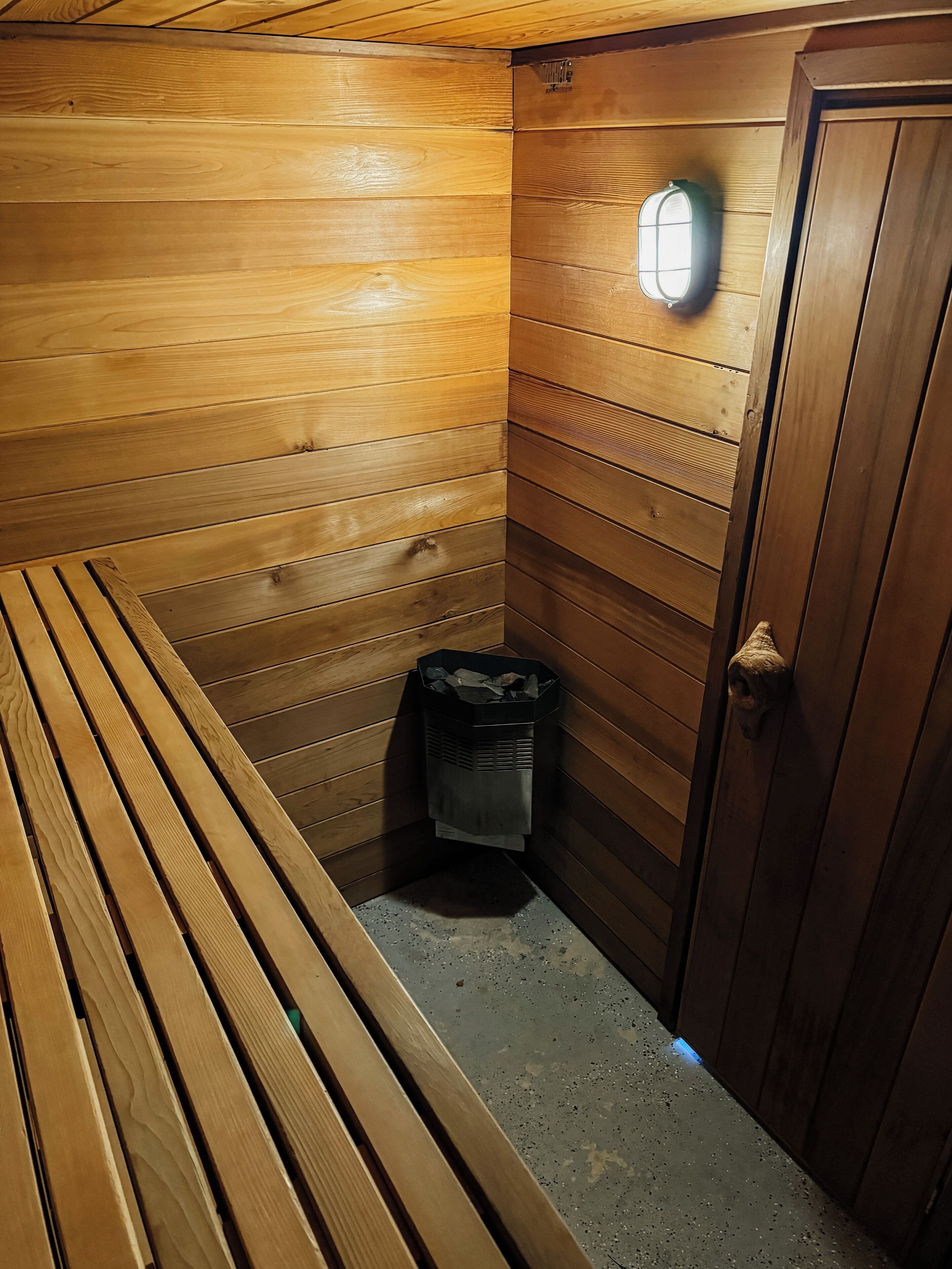 A wooden cabin with a bench, a door, and a trash bin.