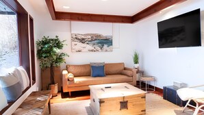 Ein modernes Wohnzimmer mit einer Couch, einer Holzkiste, einer Pflanze und einem Gemälde mit Strandmotiv.