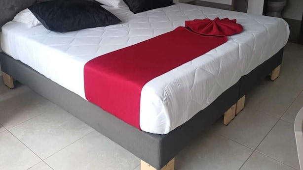 Een slaapkamer met een groot bed, een grijs gestoffeerd hoofdeinde en een schilderij van een rode roos aan de muur.