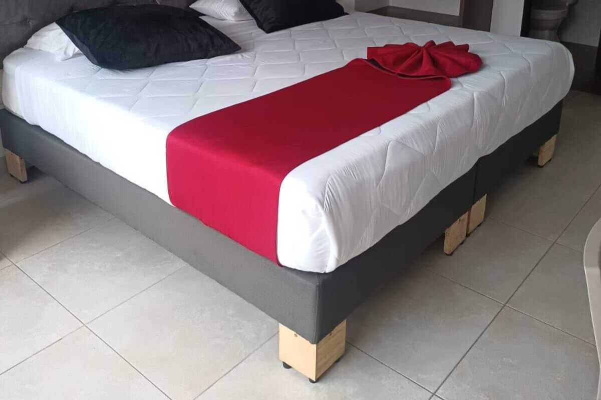 Un dormitorio con una cama grande, un cabecero tapizado en gris y un cuadro de una rosa roja en la pared.