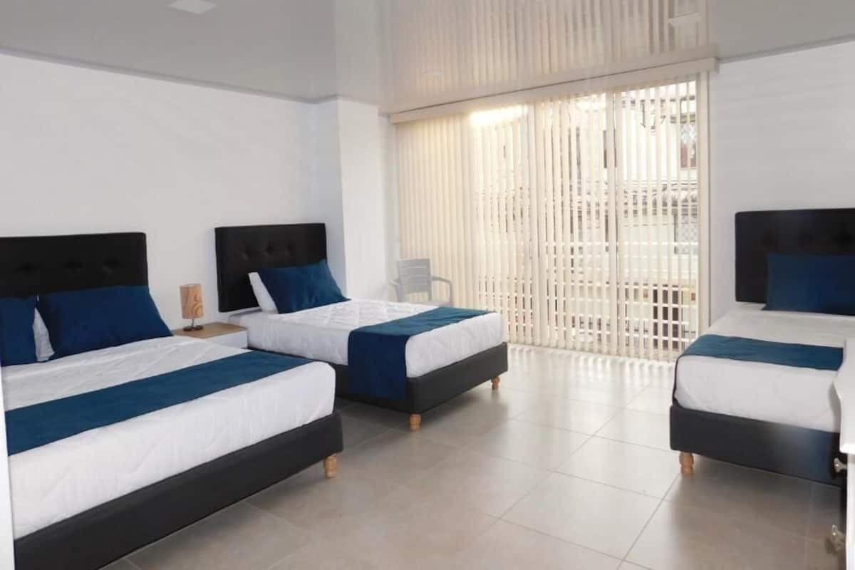 Una habitación de hotel con tres camas, cada una con cabecero negro y ropa de cama azul.