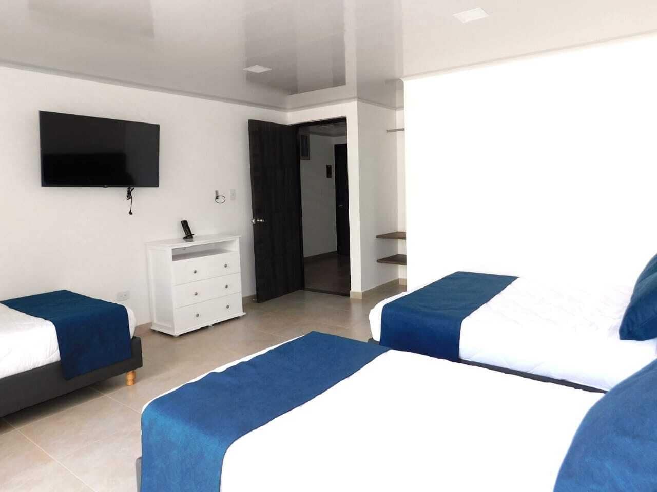 A modern hotel room with two beds, a flat-screen TV mounted on the wall, a white dresser, and a door leading to another room.