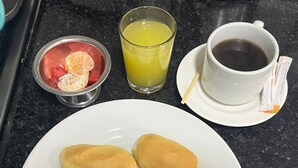Een ontbijt bord met roerei, worst en twee broodjes, vergezeld van een glas sinaasappelsap en een kop koffie.