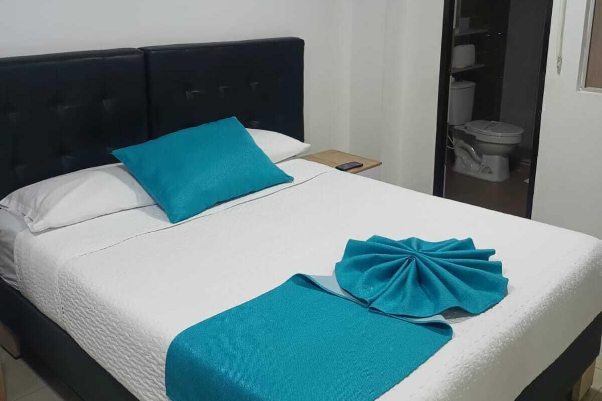 Una cama individual con cabecera negra, ropa de cama blanca y una manta turquesa.