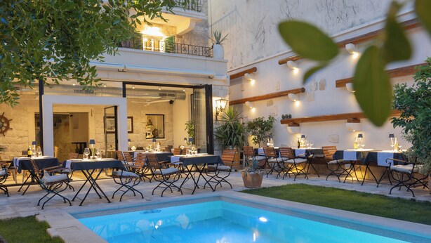 An outdoor pool area with seating and tables, surrounded by greenery and a building with a stone facade. - Casa Columba (Makarska)
