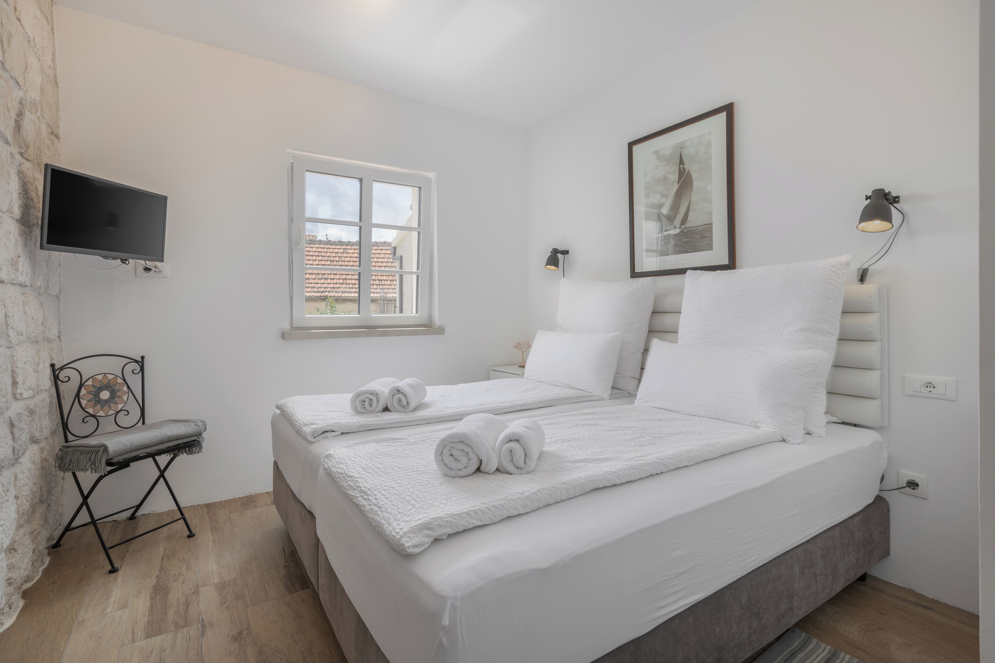 A bedroom with a bed, a TV, a window, and a wall-mounted lamp.