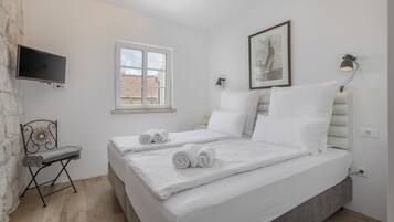 A bedroom with a bed, a TV, a window, and a wall-mounted lamp.