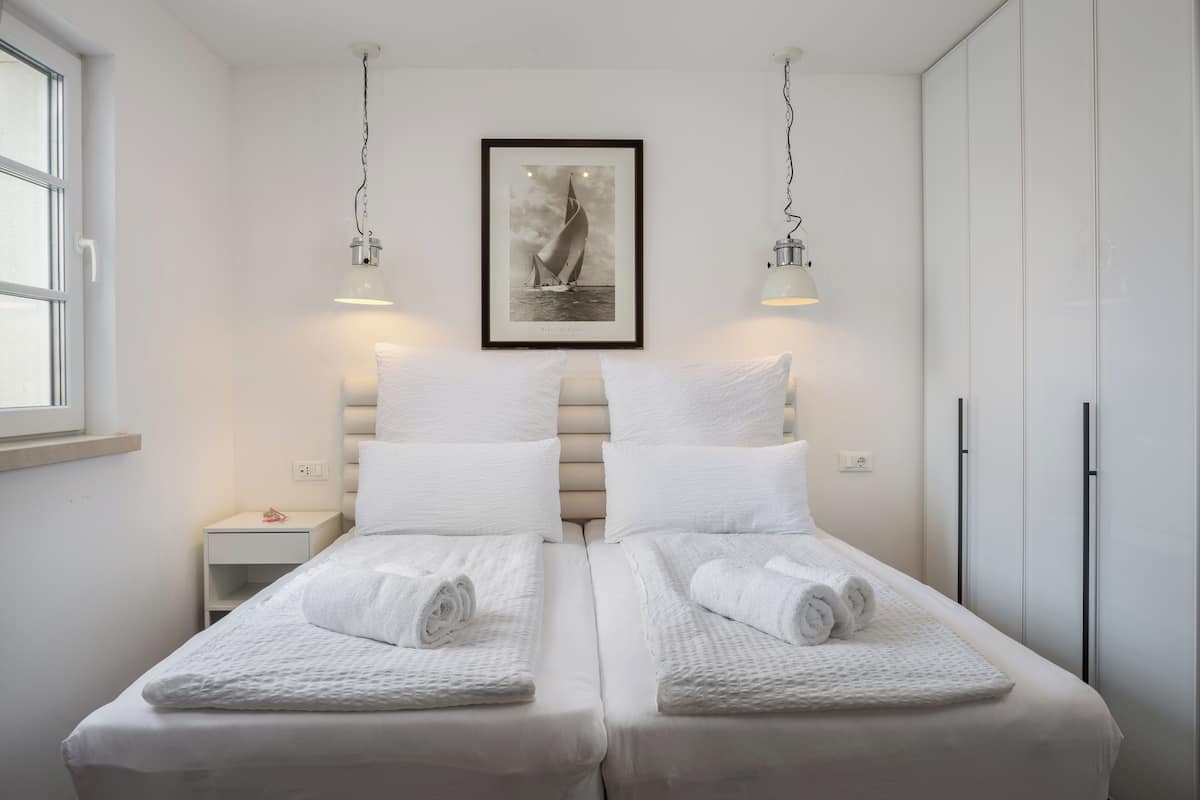 Ein Hotelzimmer mit zwei Betten, weißen Leinen, einem gerahmten Bild an der Wand und Pendelleuchten.
