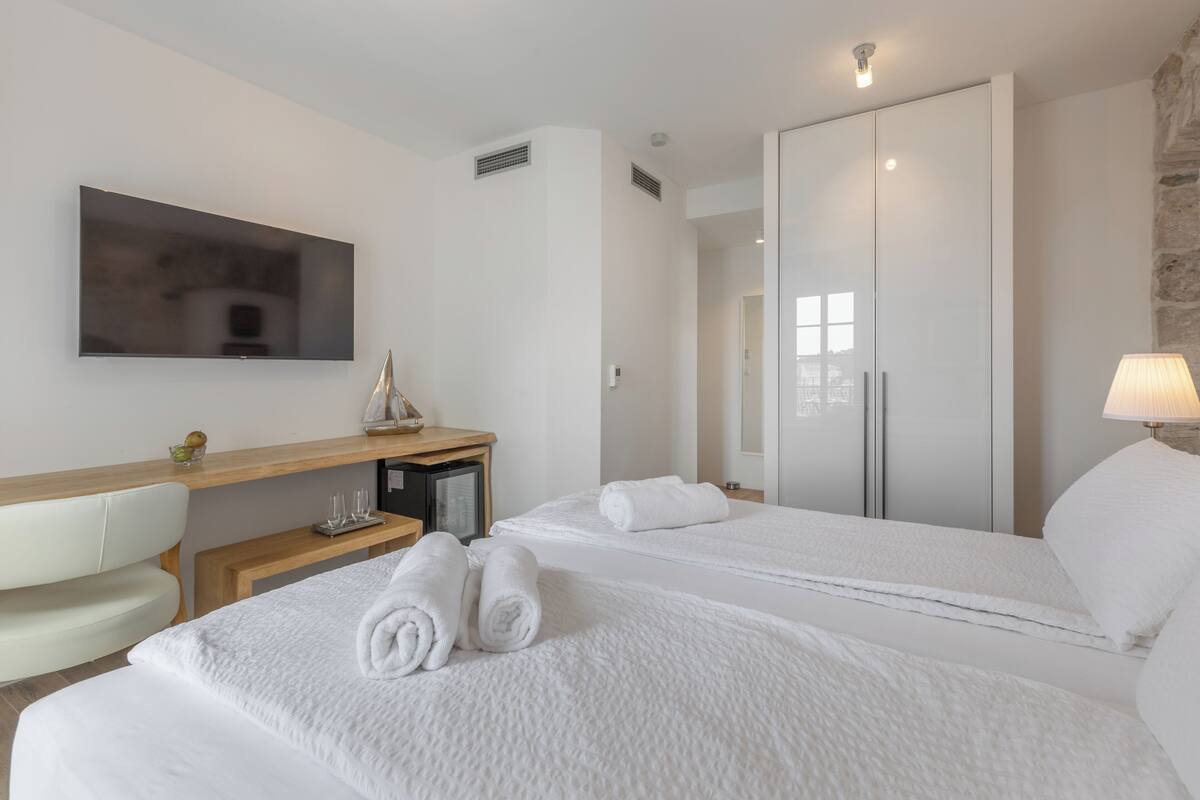Ein Hotelzimmer mit zwei Betten, einem Schreibtisch mit Computer, einem Fernseher und einem Spiegel.