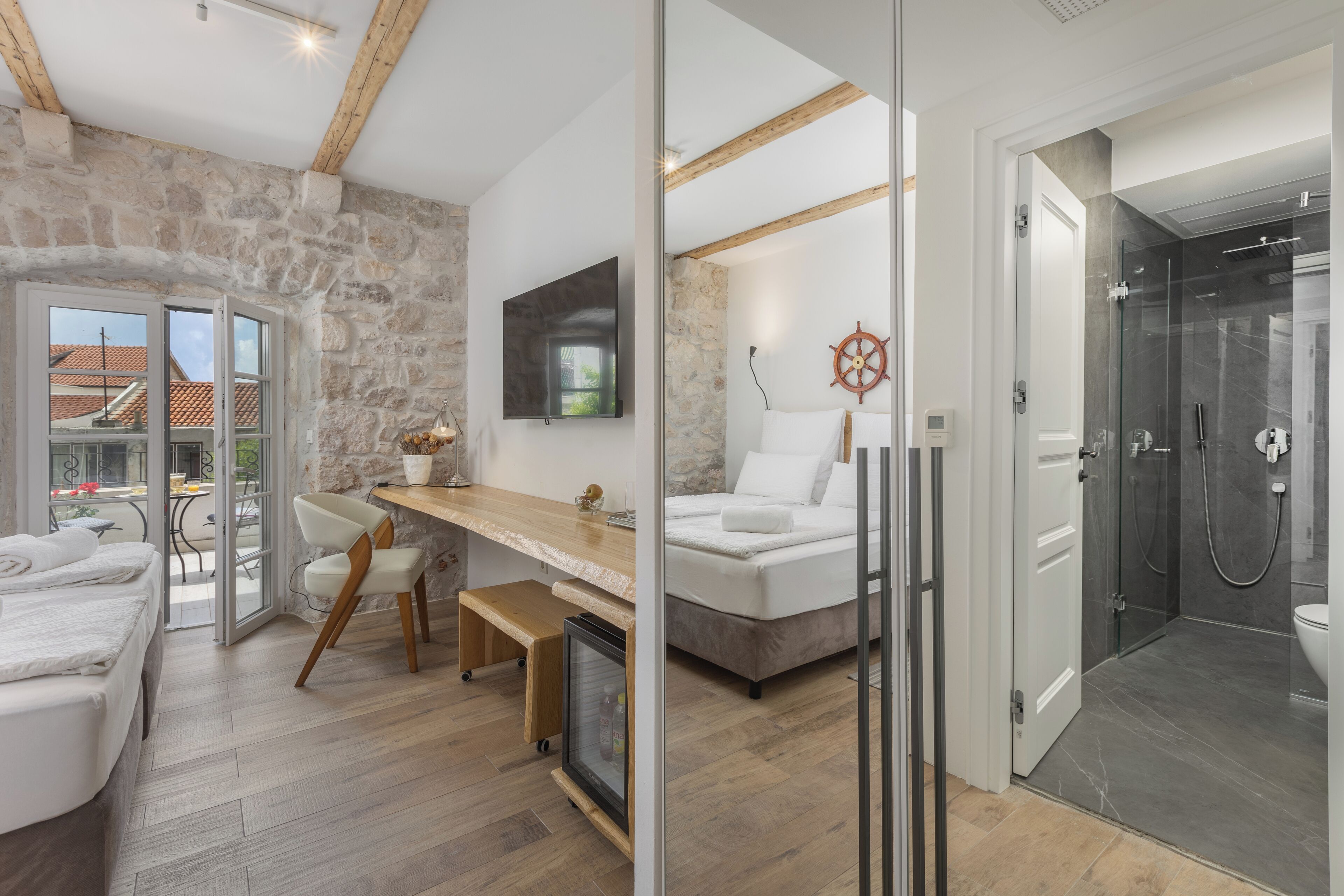Una habitación moderna con pared de piedra, techo de madera, cama, escritorio, televisor y cabina de ducha de vidrio.