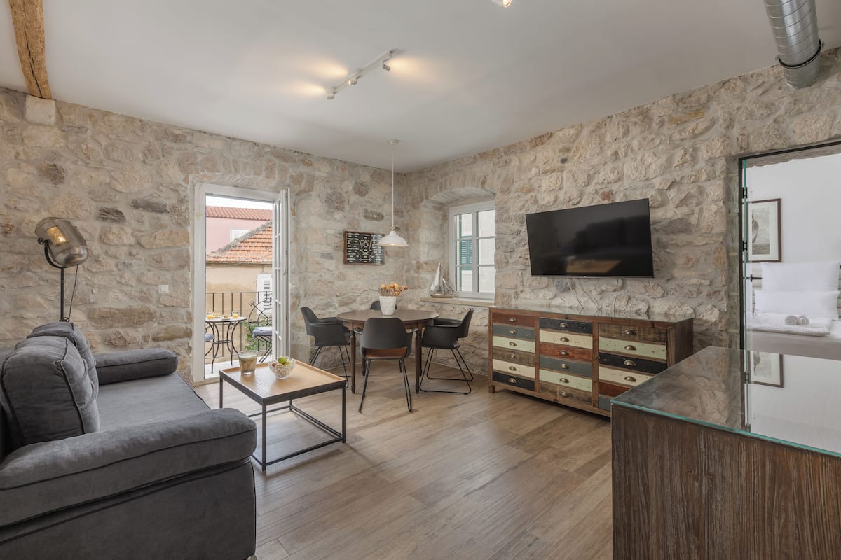 Ein Wohnzimmer mit Steinwänden, einem grauen Sofa, einem Holztisch, einem Fernseher und einem Kamin aus Stein.