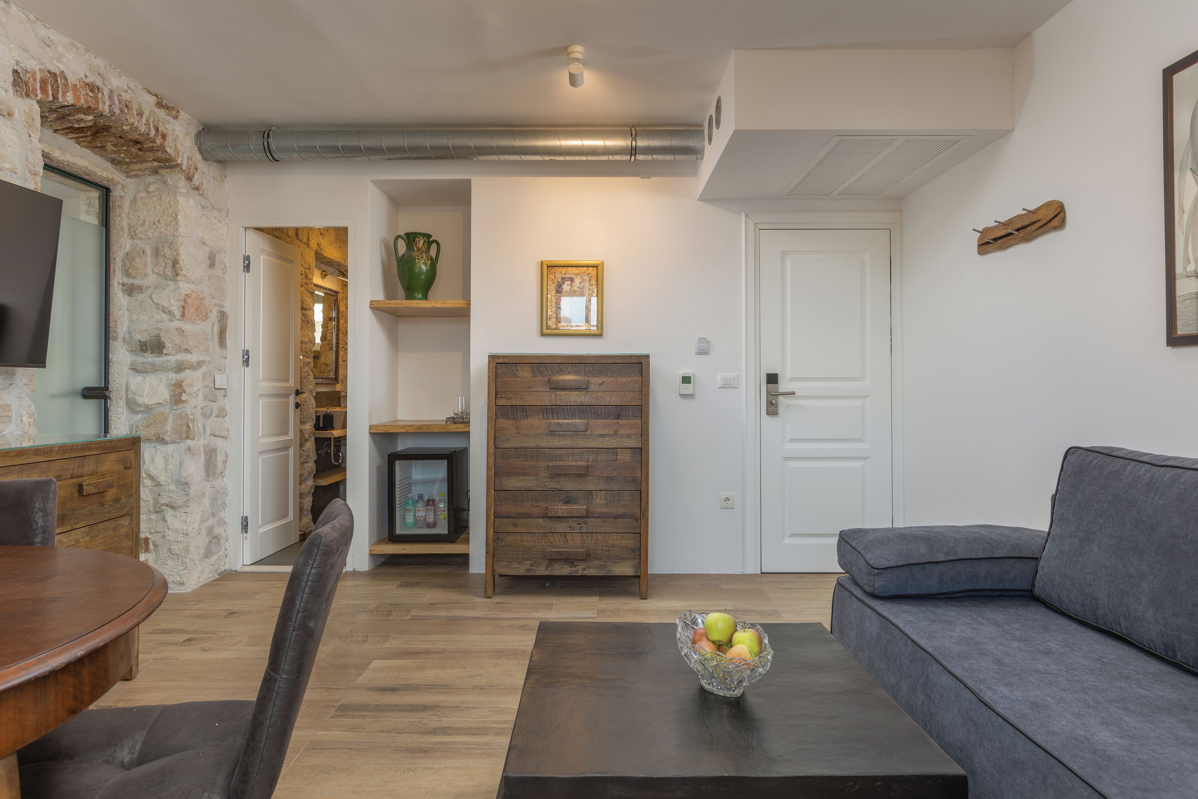Una sala moderna con una pared de acento de piedra, una mesa de comedor de madera, un sofá gris y una mesa baja con fruta.