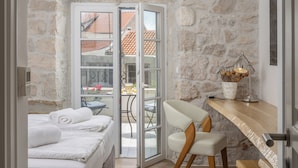 A bedroom with a stone wall, a bed with white linens, a wooden desk, and a chair. - Casa Columba (Makarska)