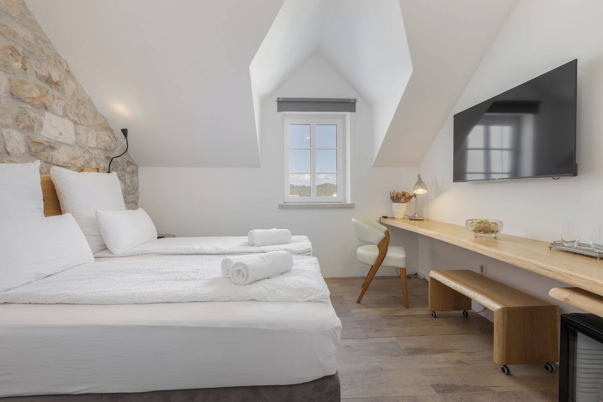 Ein modernes Schlafzimmer mit einer Loft-Decke, einem Bett mit weißer Bettwäsche, einem Schreibtisch mit Stuhl und einem an der Wand montierten Flachbildfernseher.