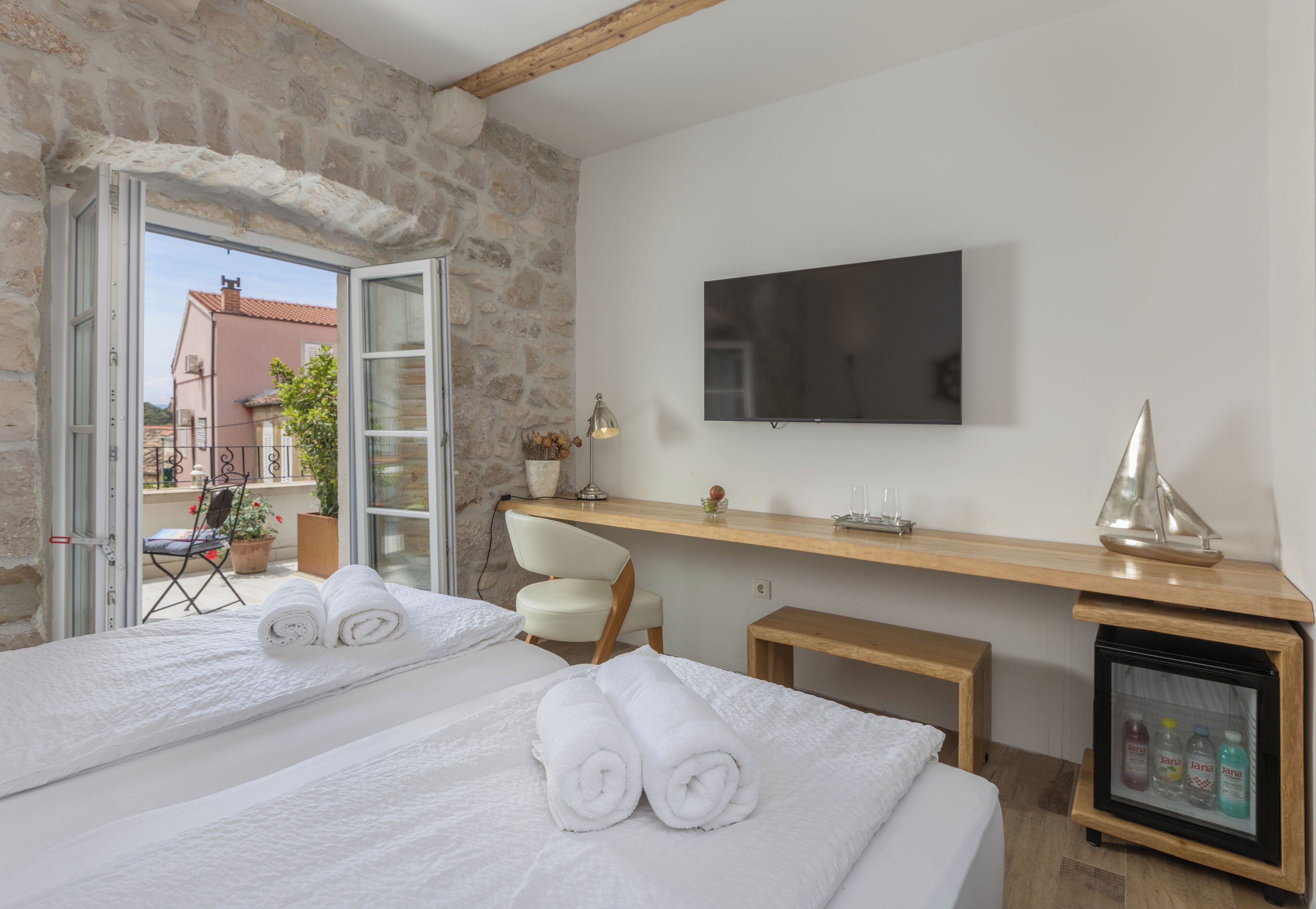 Habitación de hotel con dos camas, televisión, una mesita de noche con lámpara, un modelo de barco y un minibar.