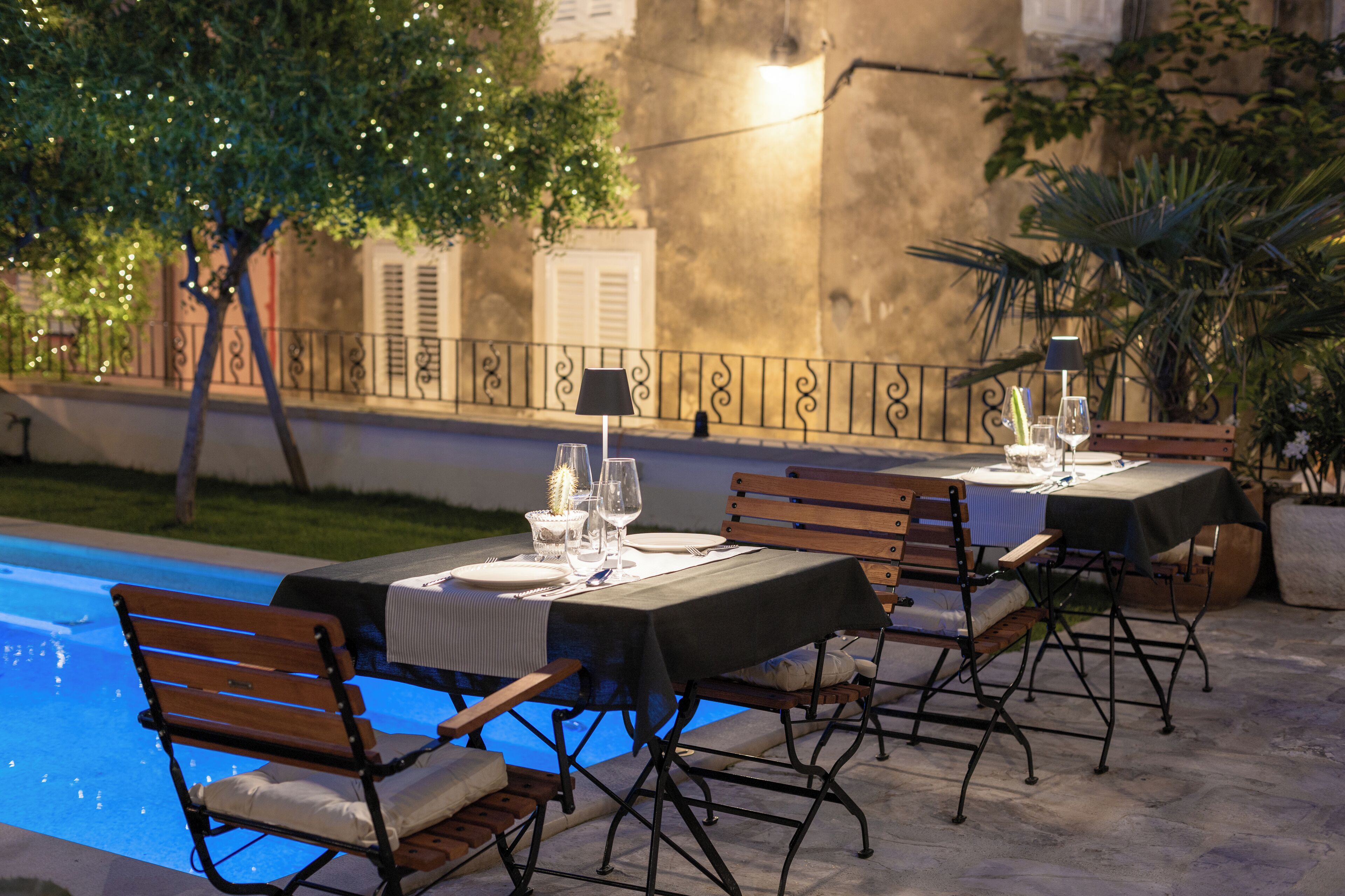 Un área de comedor al aire libre con mesas dispuestas para dos, bancos y una piscina.