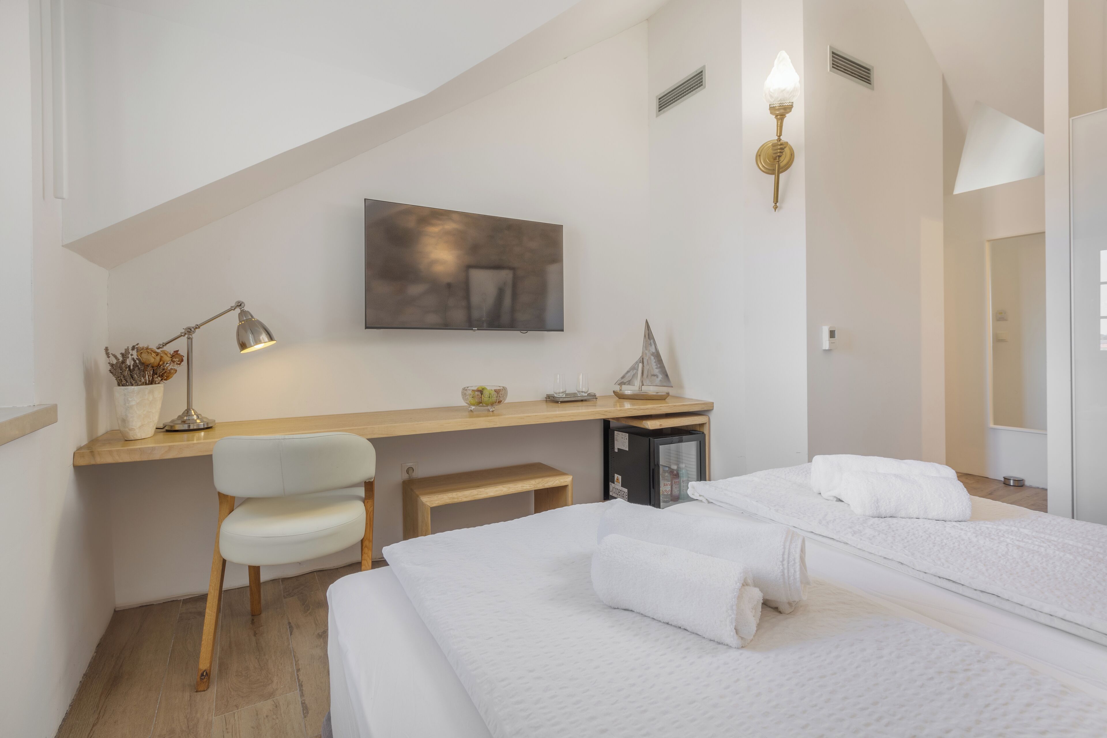 A hotel room with a bed, a desk, a chair, a TV, and a small kitchenette.