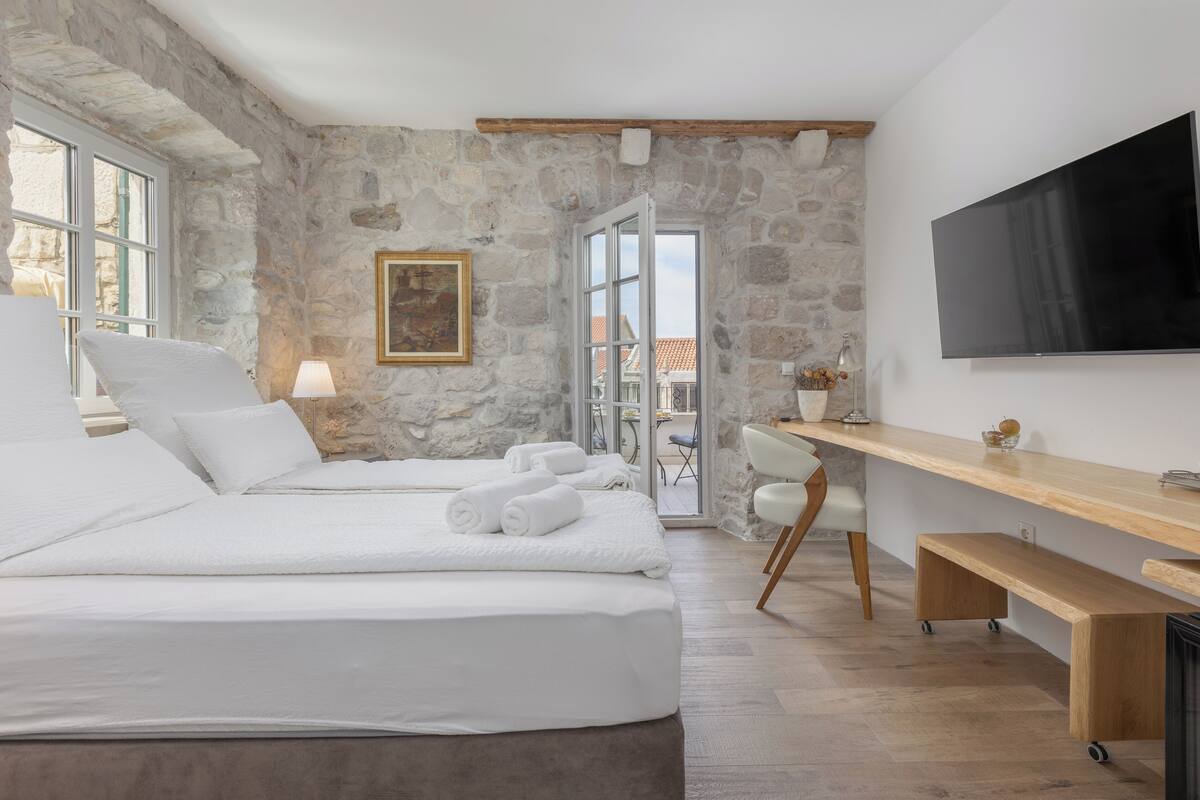Ein Schlafzimmer mit Stehwänden, einem Bett mit weißen Leinentüchern, einem Fernseher und einem Holztisch.