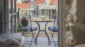 A balcony with a table and chairs, a view of buildings with red roofs, and a stone wall. - Casa Columba (Makarska)