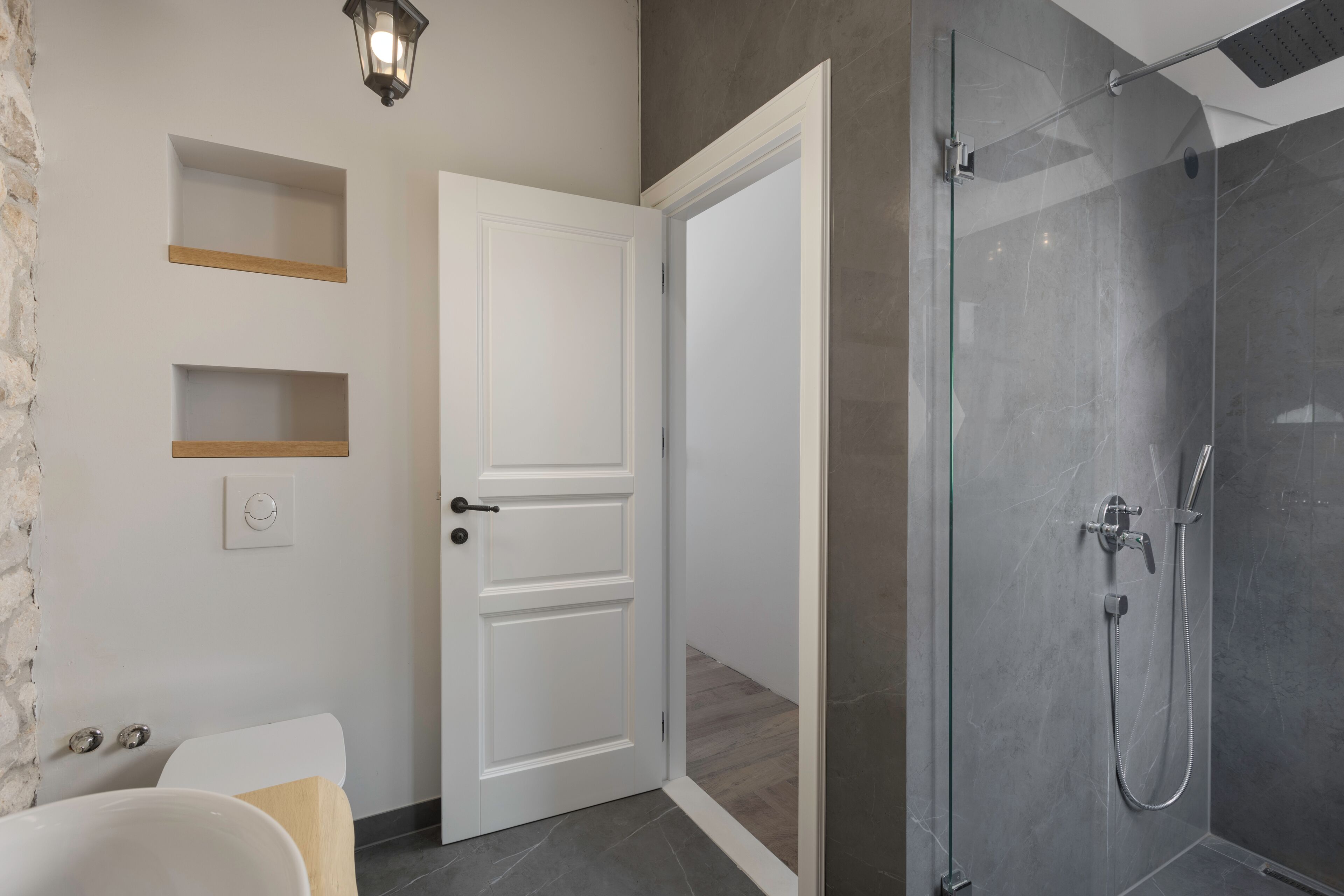 A modern bathroom with a glass shower enclosure, a white bathtub, and a door leading to another room.