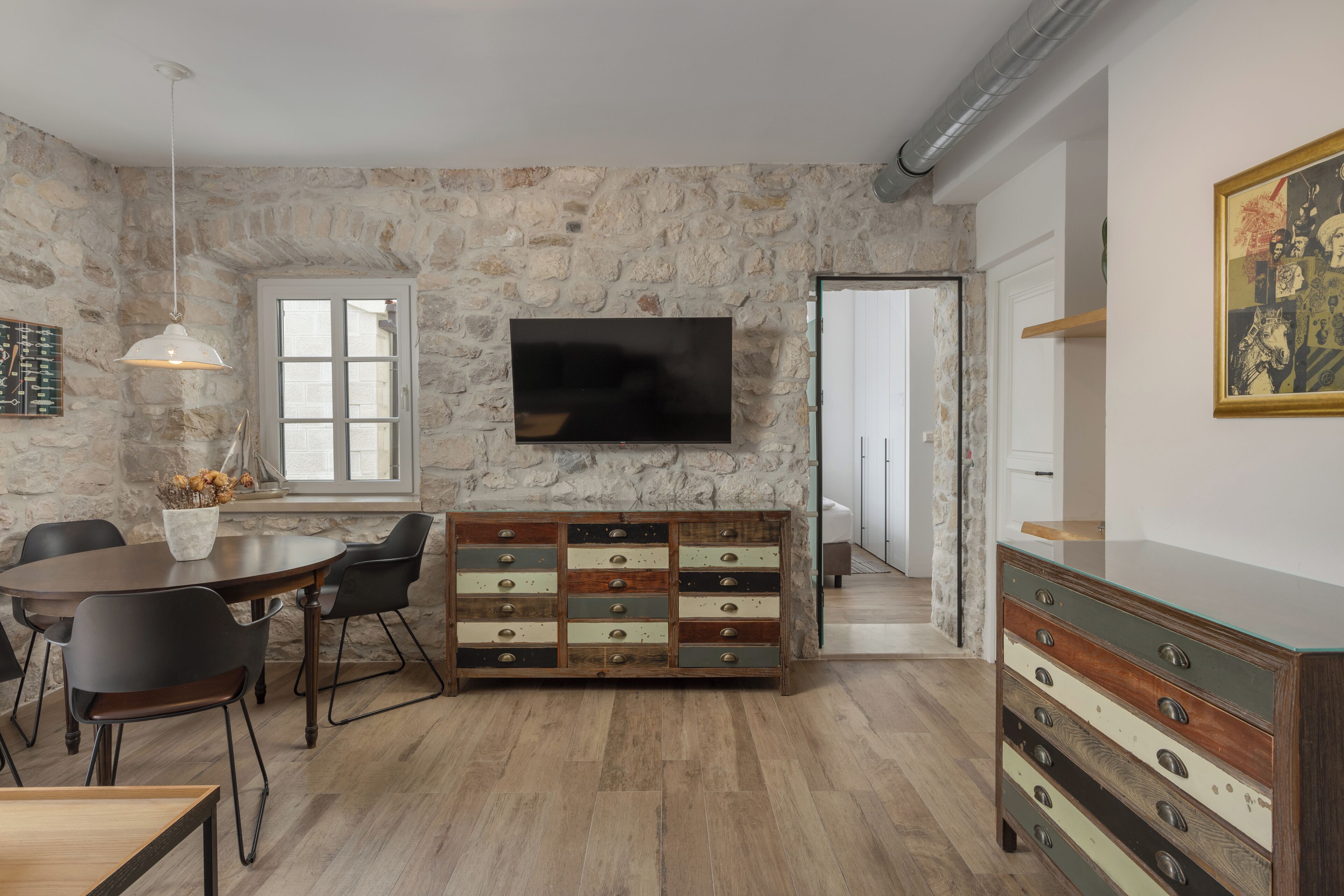 Una sala moderna con pared de piedra, un televisor de pantalla plana, una mesa de comedor de madera con sillas y un mueble de varios cajones.