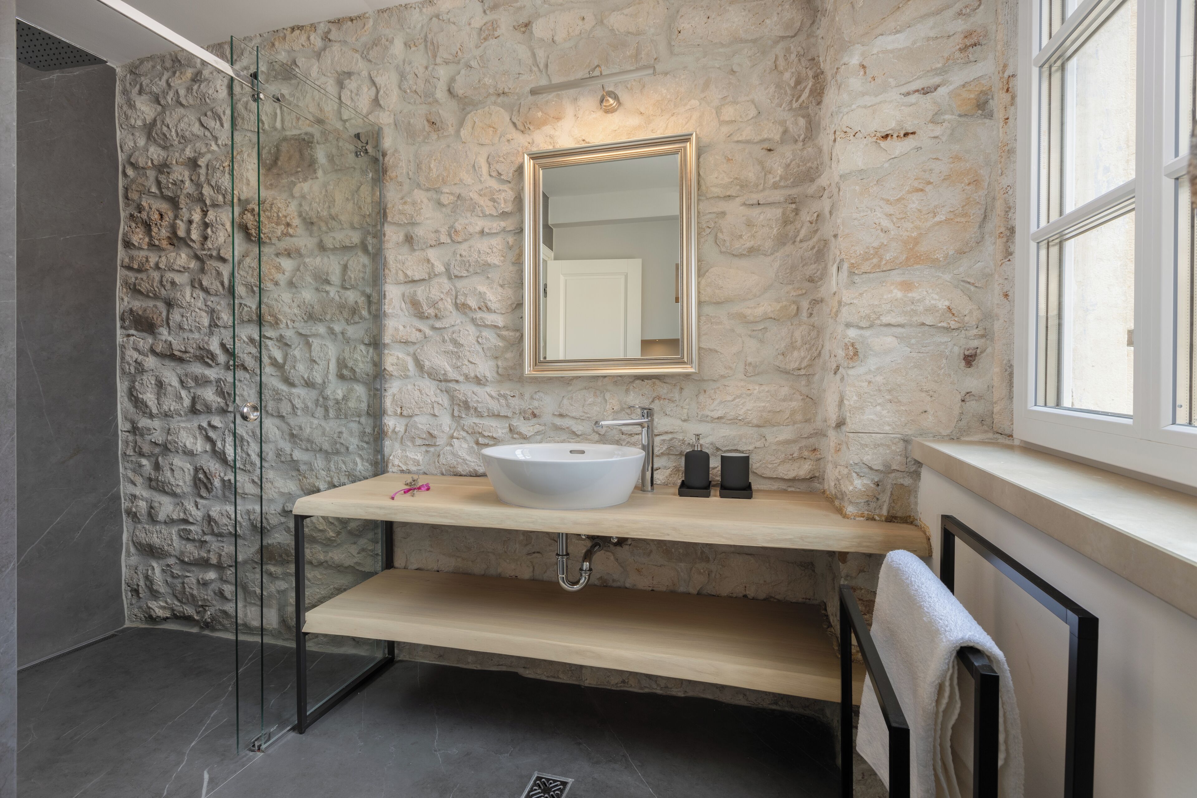 Un baño con pared de piedra, un lavabo blanco y un espejo.