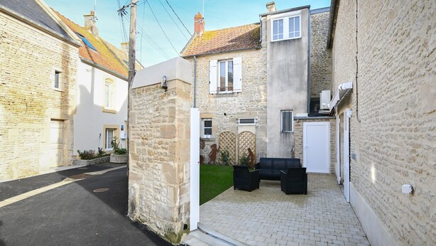 A narrow street with stone buildings, a paved courtyard, and a black outdoor seating area. - La Maison des Ours - proche plage de Courseulles (Courseulles-sur-Mer)