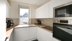 A modern kitchen with white cabinets, a granite countertop, a window, and a built-in oven. - La Maison des Ours - proche plage de Courseulles (Courseulles-sur-Mer)