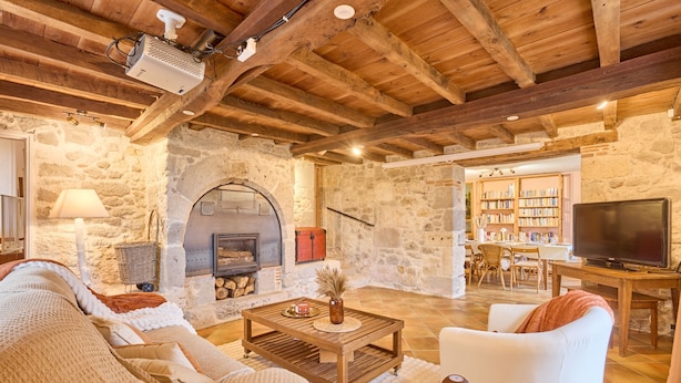 A cozy living room with a stone fireplace, wooden beams, a television, and a bookshelf. - Pierre Idyllique - Climatisée avec grand jardin (Saumont)