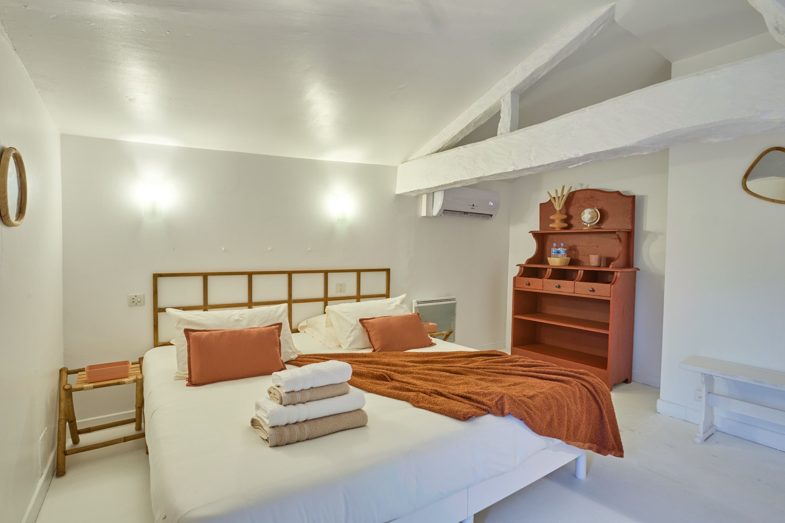 Een keurig opgemaakt slaapkamer met een bed, nachtkastjes, een houten dressoir en een wandplank.