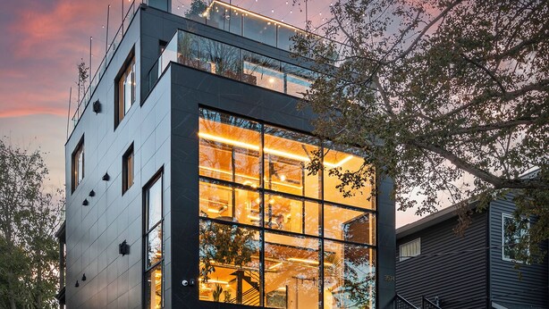 A modern two-story building with large windows and a glass facade, surrounded by a well-maintained garden and a street.